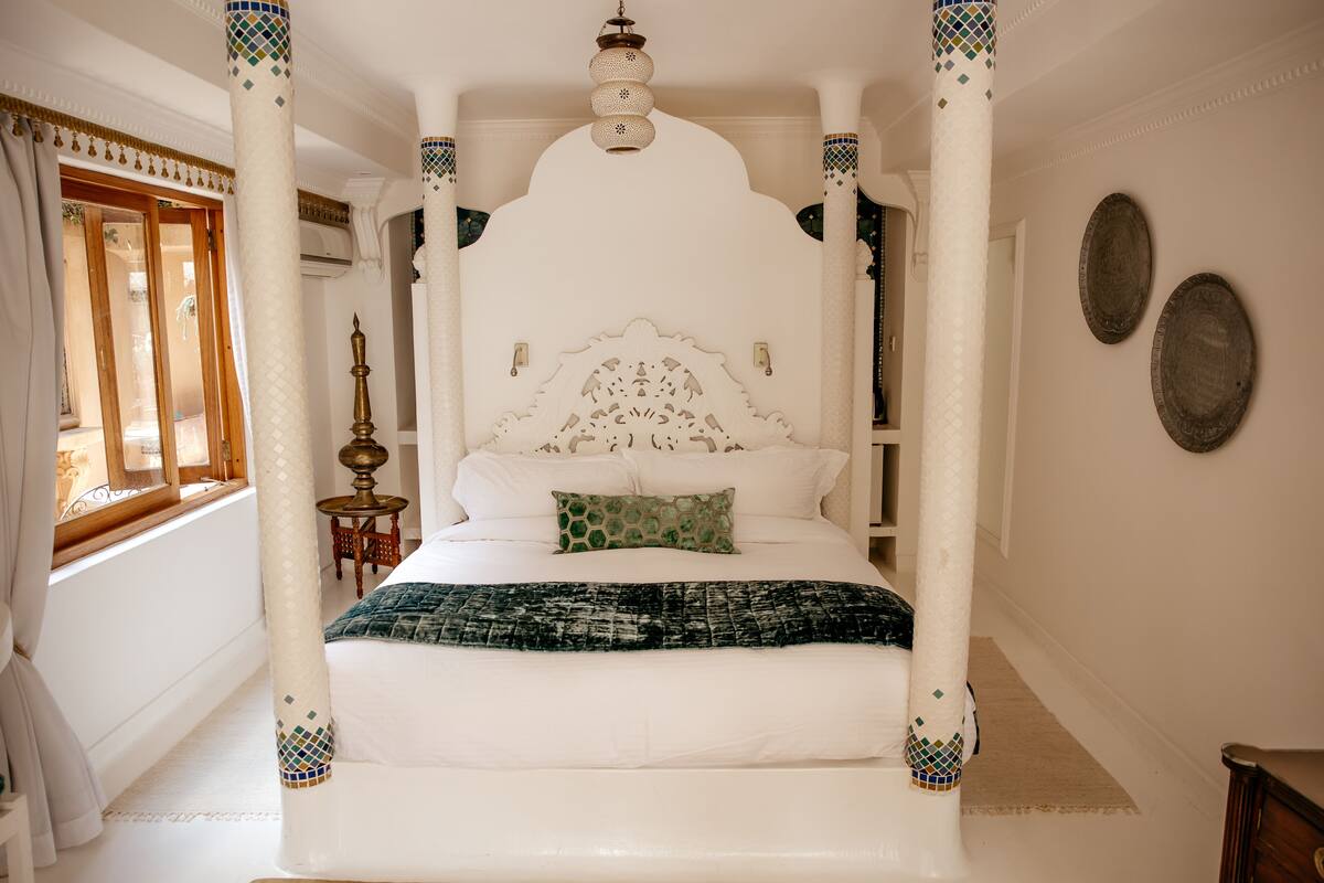 Uma cama de dossel com um toldo branco, um travesseiro verde e um cobertor estampado.