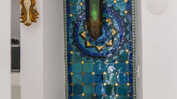 A room with a decorative tile wall, a small shelf with a teapot, cups, and a kettle.