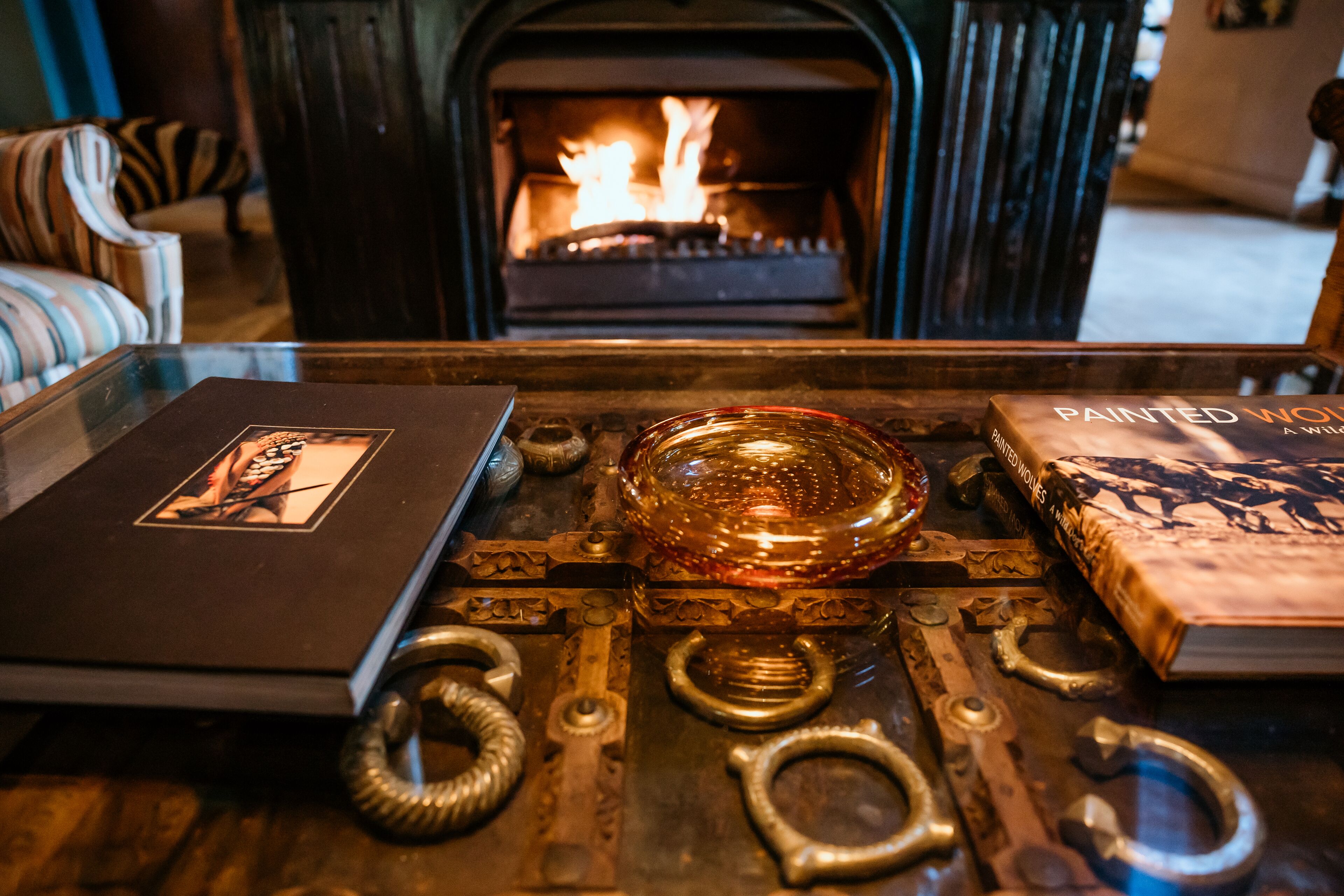 A fireplace with a fire, a glass bowl, and two books on a wooden table.