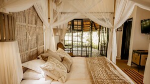 A bedroom with a bed, white curtains, a wooden headboard, and a television on the wall.
