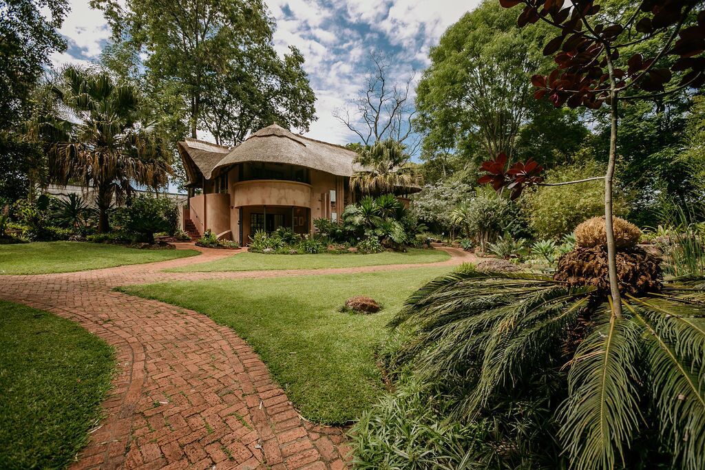 A bungalow with a thatched roof, surrounded by lush greenery and a brick pathway.