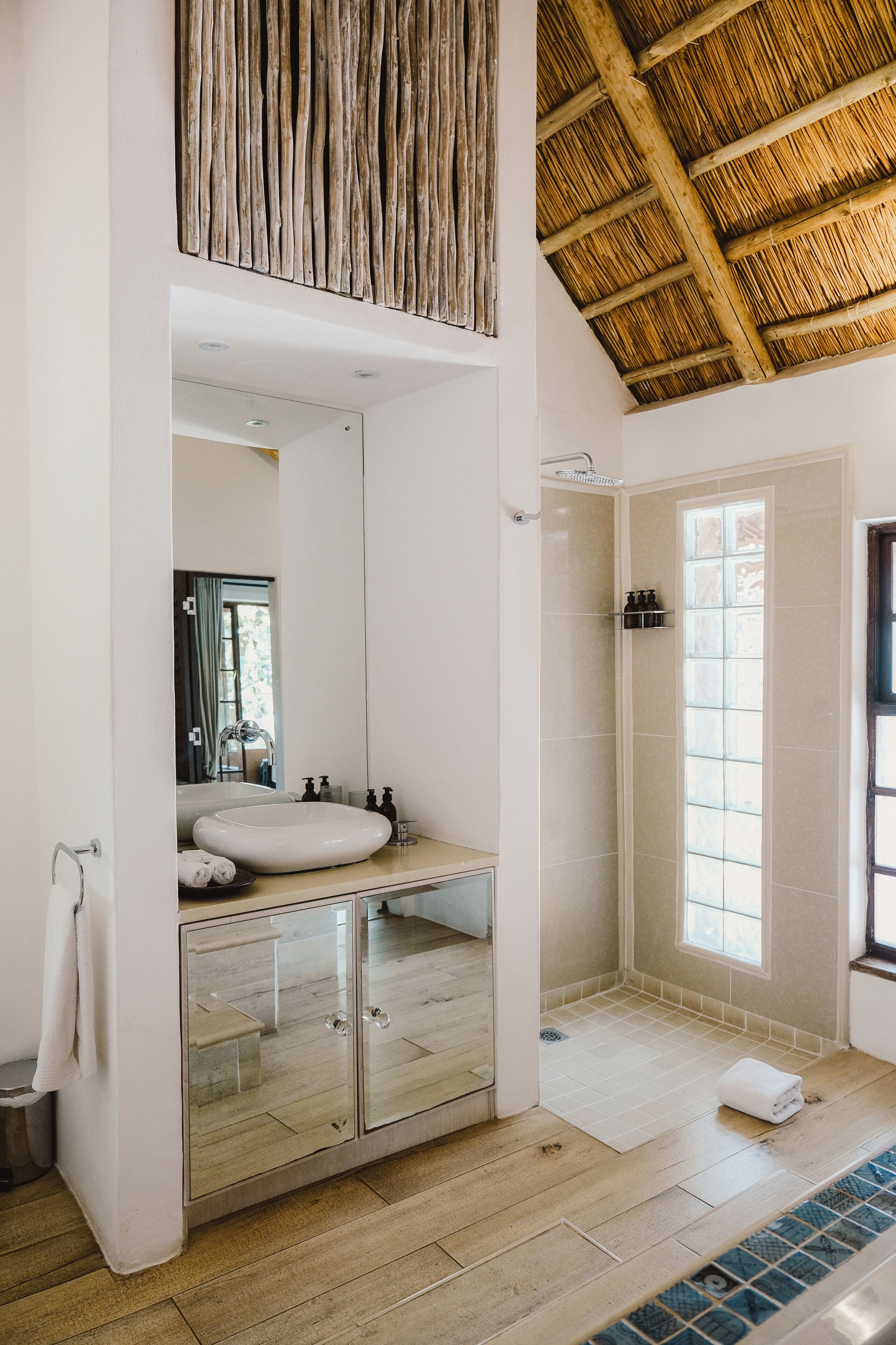 A modern bathroom with a large mirror, a sink, a shower, and a wooden ceiling.