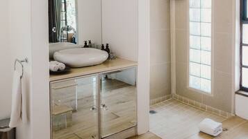 A modern bathroom with a large mirror, a sink, a shower, and a wooden ceiling.