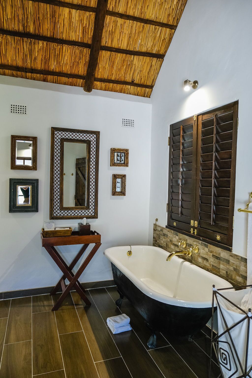 A bathroom with a large bathtub, a wooden vanity, a mirror, and a window with shutters.