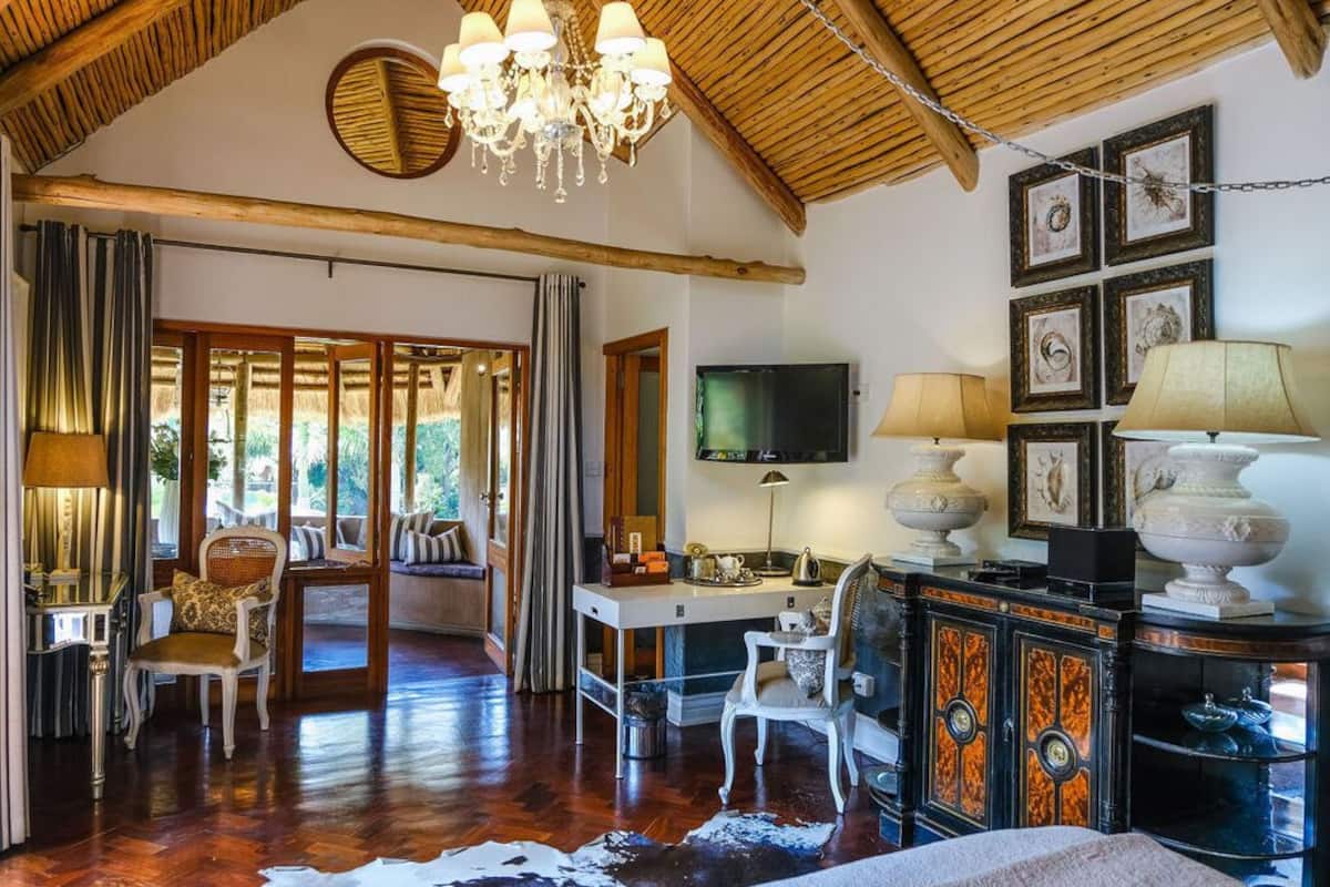 Um quarto amplo com teto de madeira, um lustre, uma televisão e uma escrivaninha com abajur.