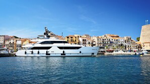 A large white yacht docked at a marina with a backdrop of colorful buildings and a clear blue sky. - Camping Les Castors (Calvi)