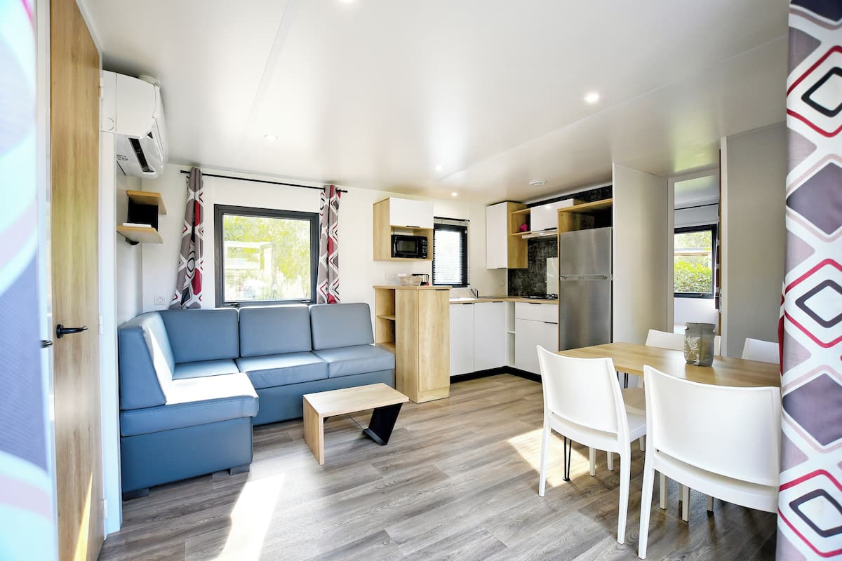 A compact living space with a sofa, dining table, chairs, a small kitchen area, and a window with curtains.