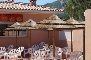 A restaurant with outdoor seating, thatched umbrellas, and a sign advertising pizzas. - Camping Les Castors (Calvi)
