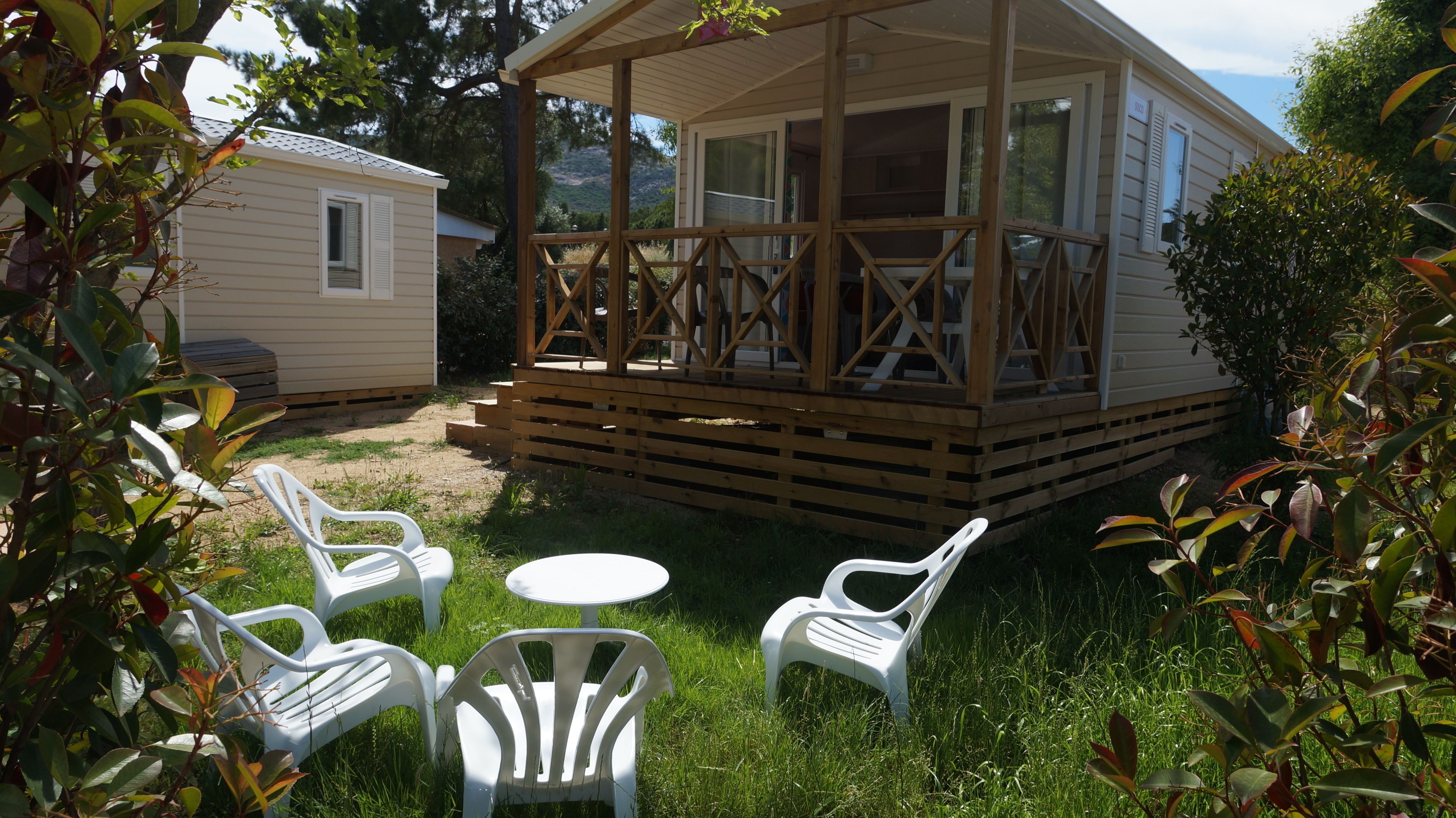 A wooden deck with a covered seating area, a small table, and white plastic chairs.
