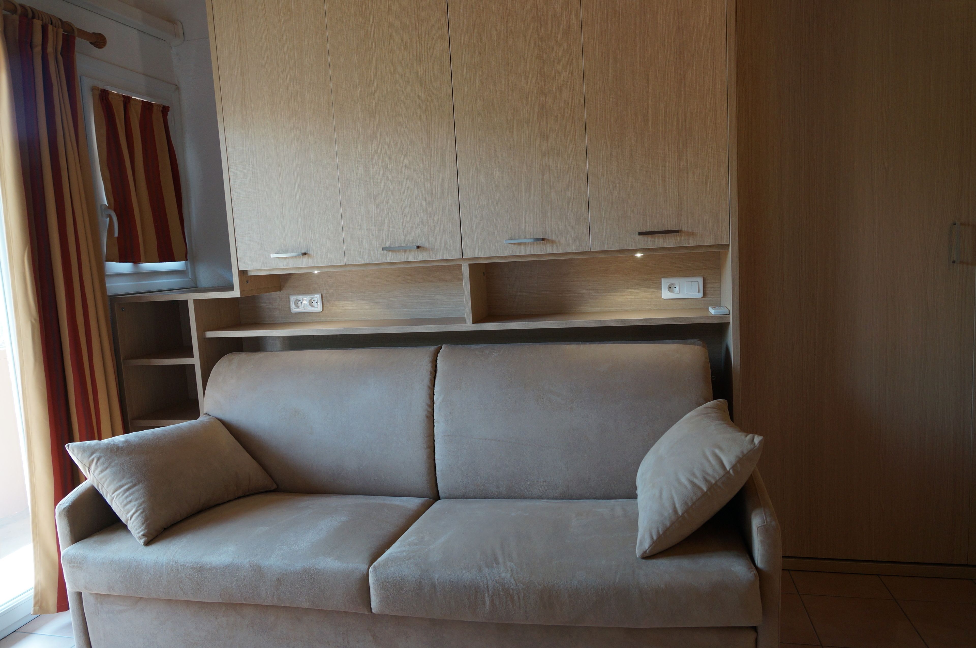 Een moderne woonkamer met een beige bank, houten kasten en een raam met gordijnen.