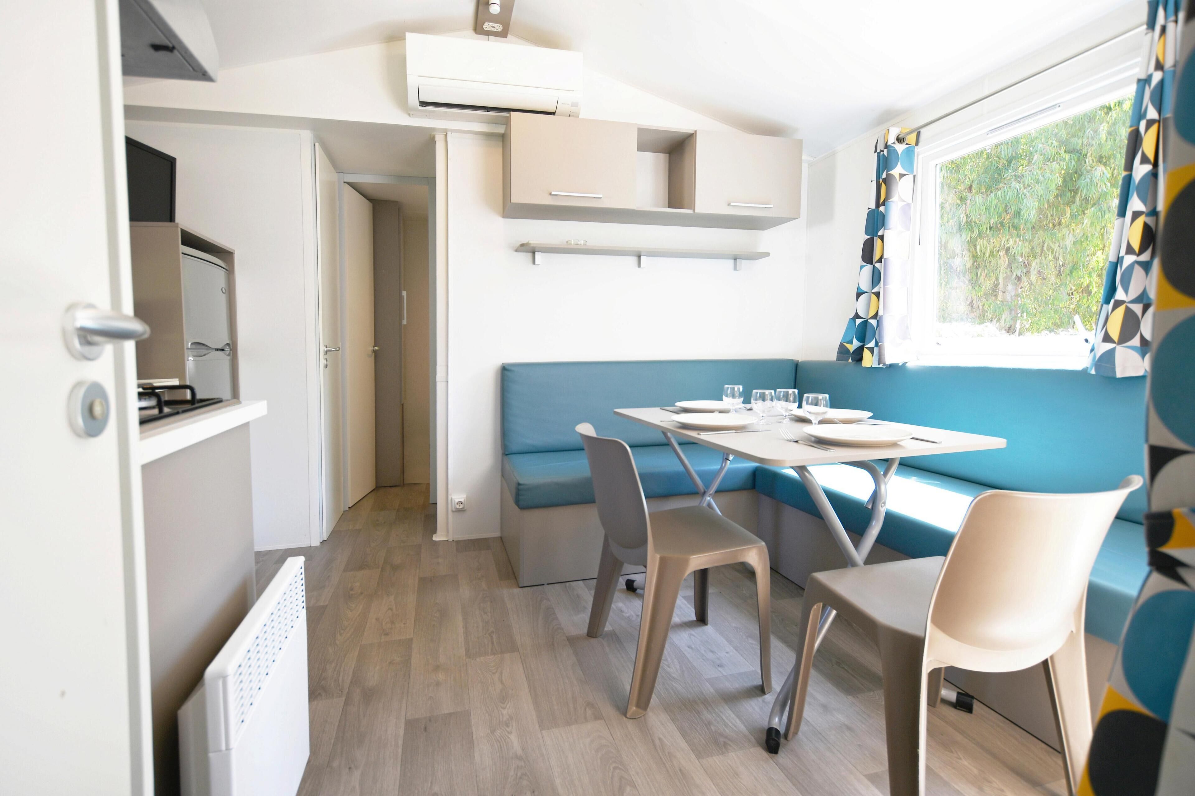 A compact kitchen with a built-in stove, a dining area with a table and chairs, and a window with curtains.