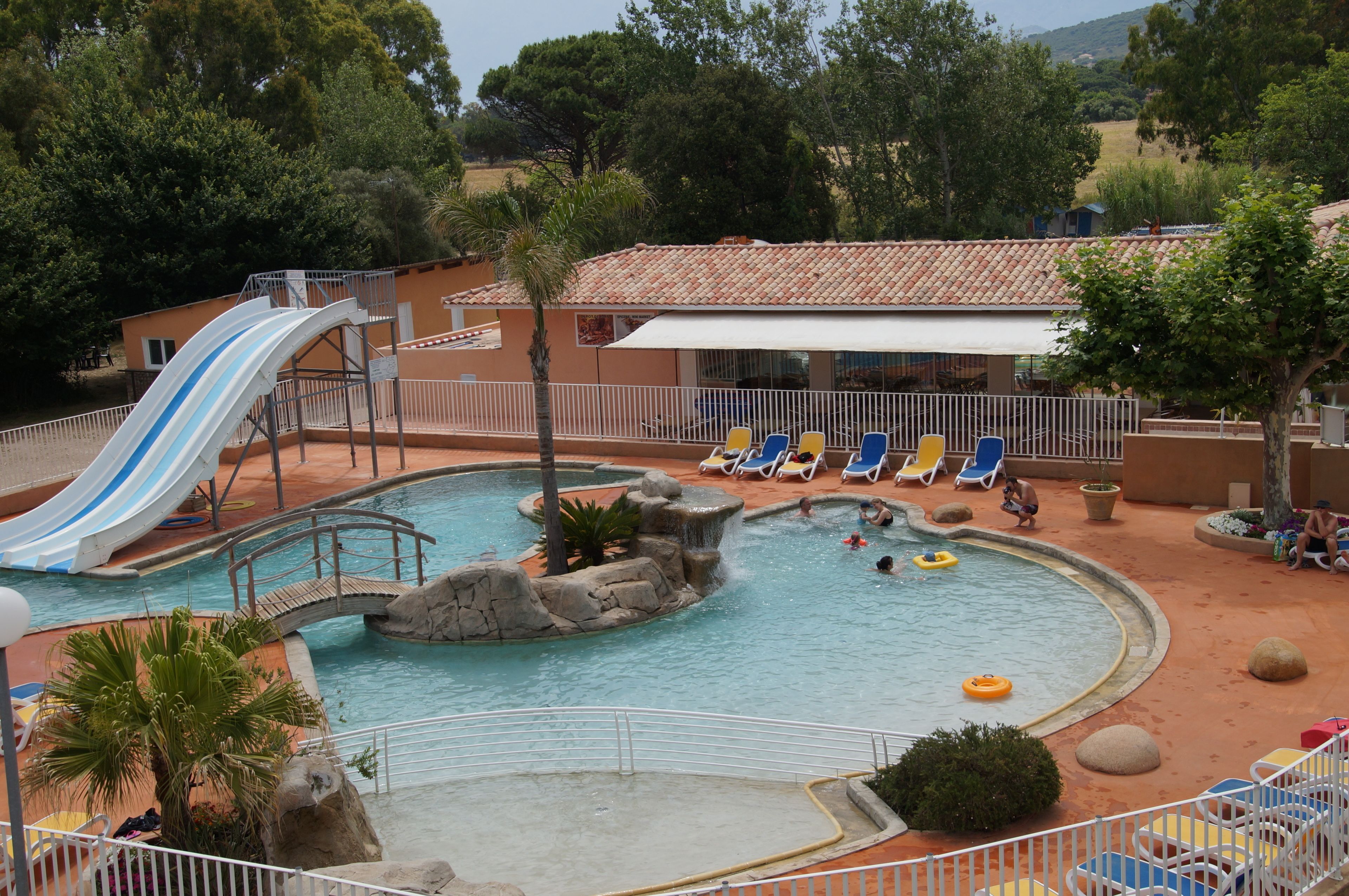 Un área de piscina con tobogán, sillas de descanso y un pequeño puente.