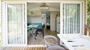 A compact, well-lit room with a dining area, kitchenette, and a sliding glass door leading to an outdoor space. - Camping Les Castors (Calvi)