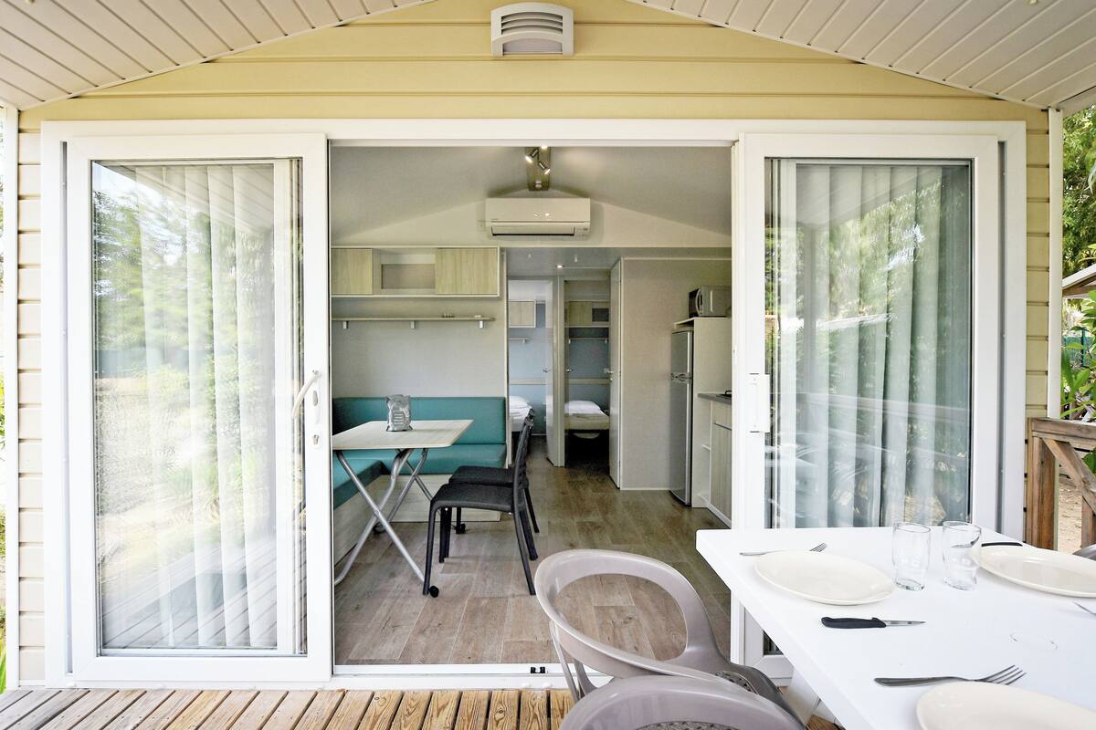 A compact, well-lit room with a dining area, kitchenette, and a sliding glass door leading to an outdoor space.