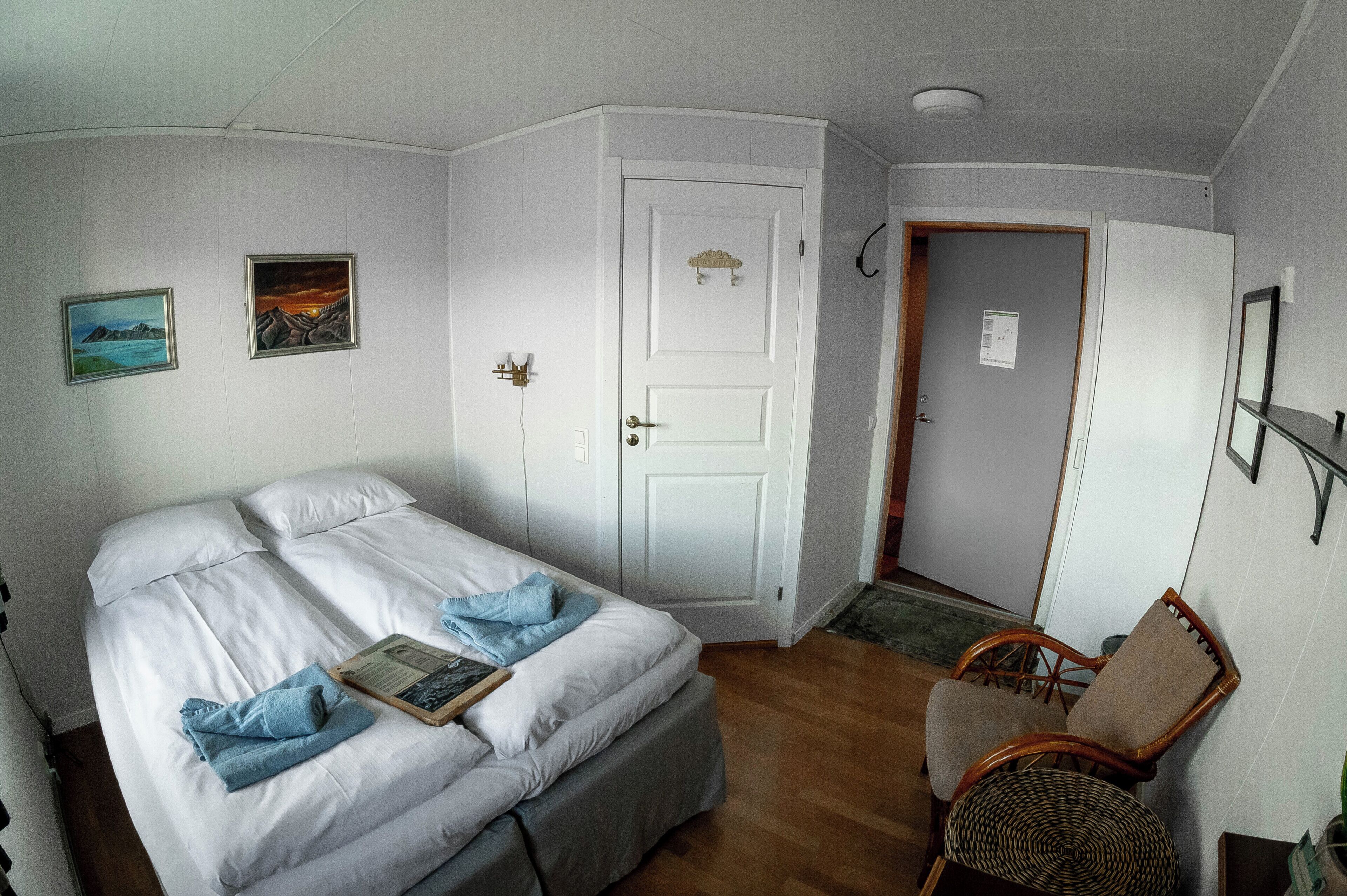 A bedroom with a bed, a chair, and two paintings on the wall.
