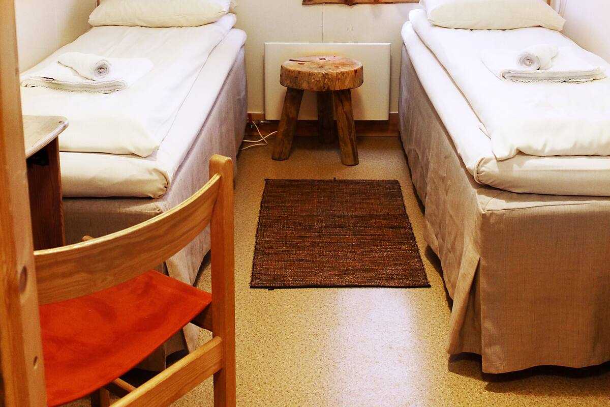 A compact room with two single beds, a small wooden table, a chair, and a window with curtains.