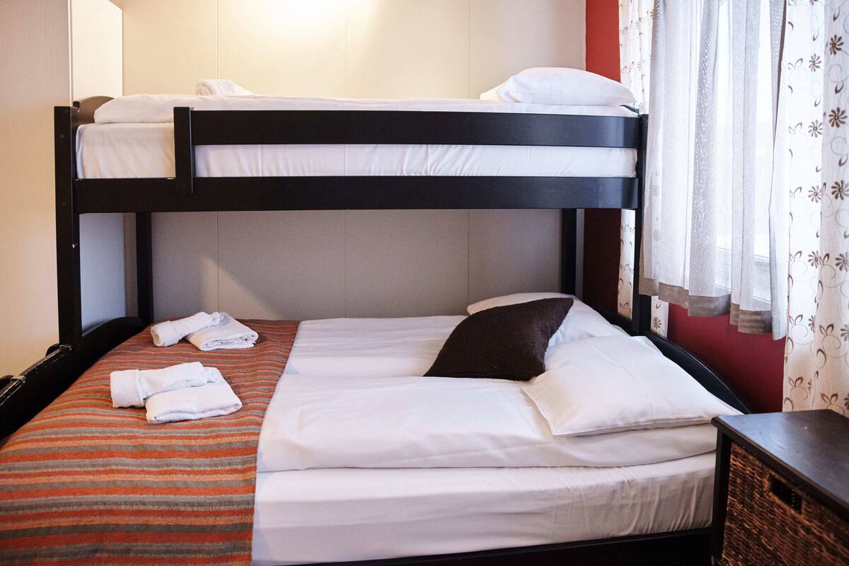 A bunk bed with white bedding and a striped orange and gray bedspread.