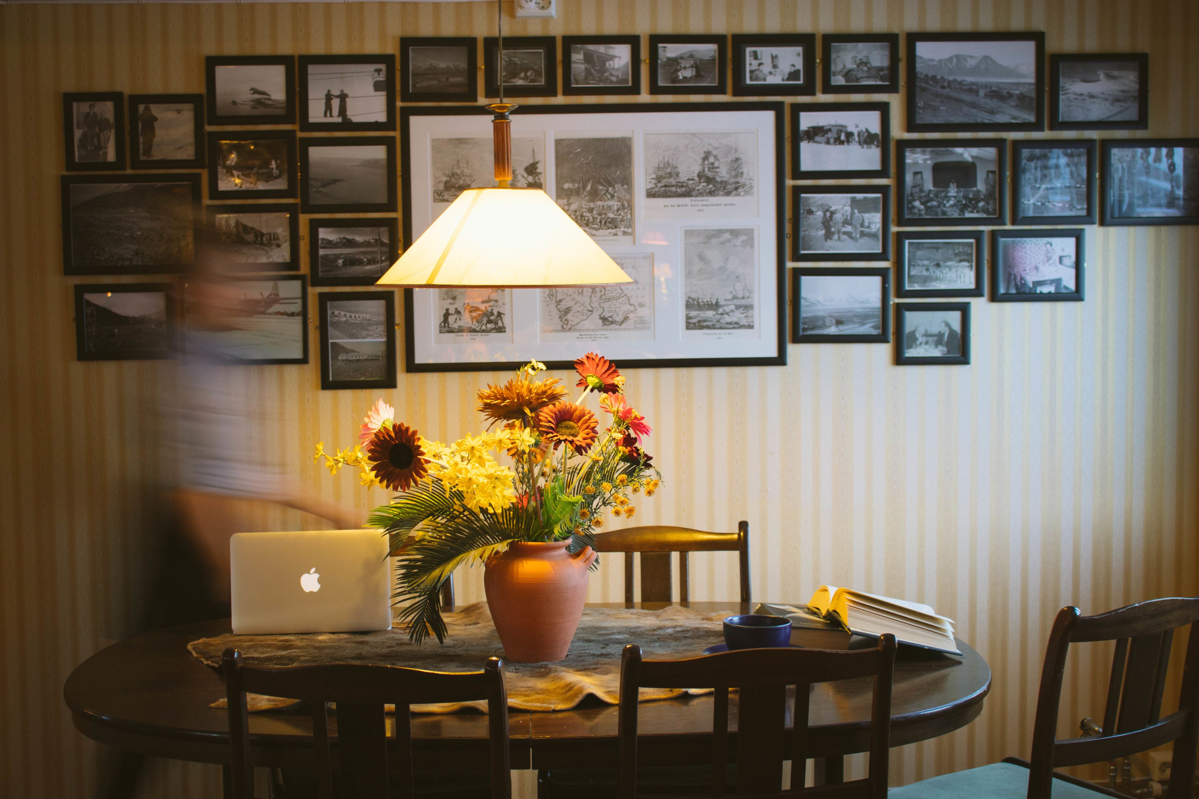 A dining table with a laptop, a vase of flowers, and a lamp.
