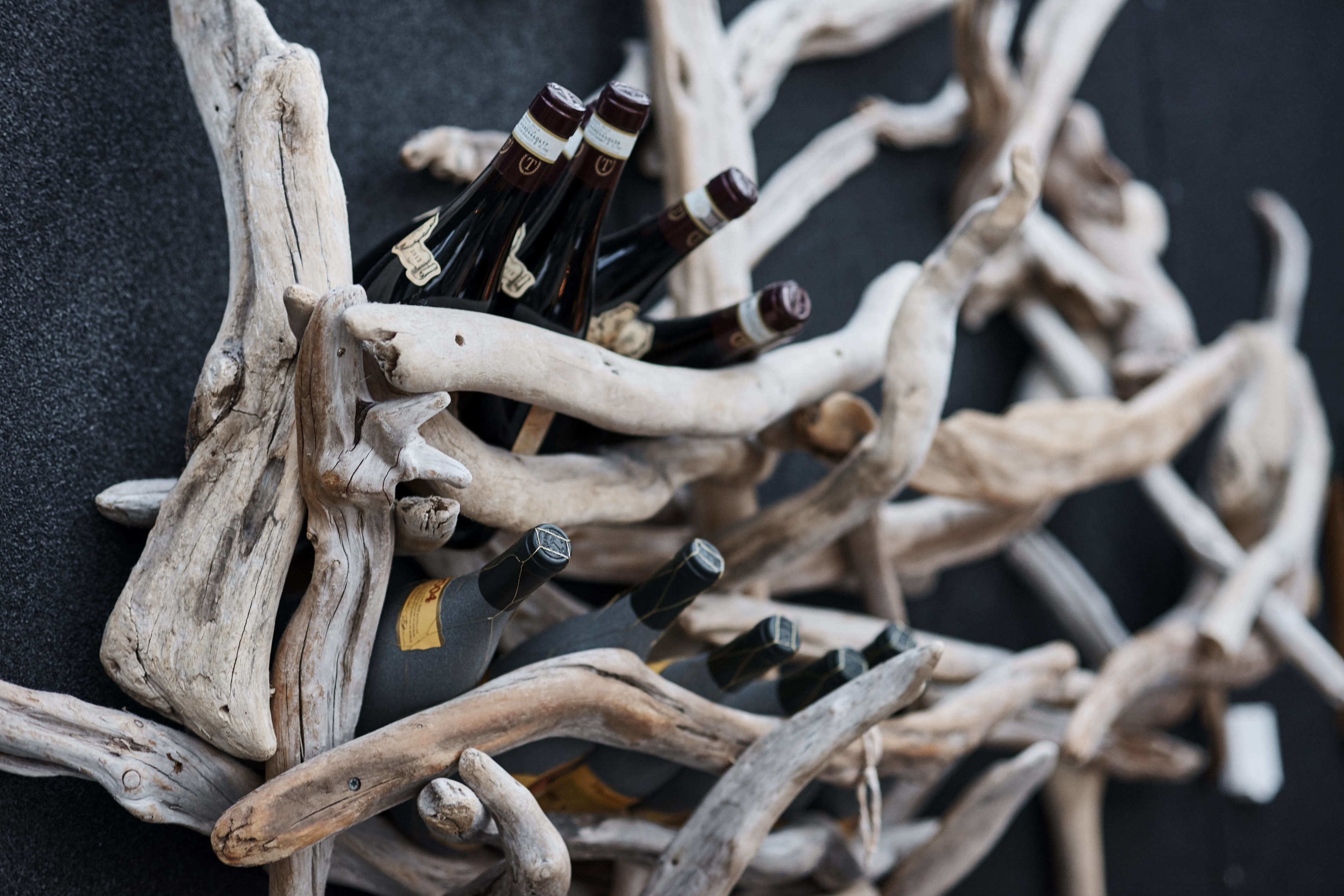 A collection of wine bottles with labels, surrounded by natural wood branches.