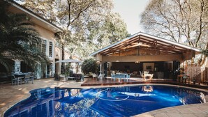 Una piscina con cubierta de madera, rodeada de mobiliario exterior y árboles.
