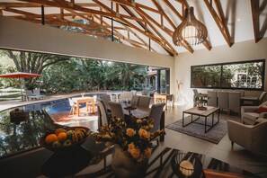 A modern living room with a large window, a pool, and outdoor seating. - Sandalwood Lodge (Harare)