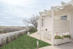 A white outdoor patio with a pergola, a table and chairs, and a planter with flowers.