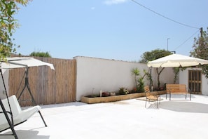 An outdoor patio area with a wooden fence, a white wall, and a bench.