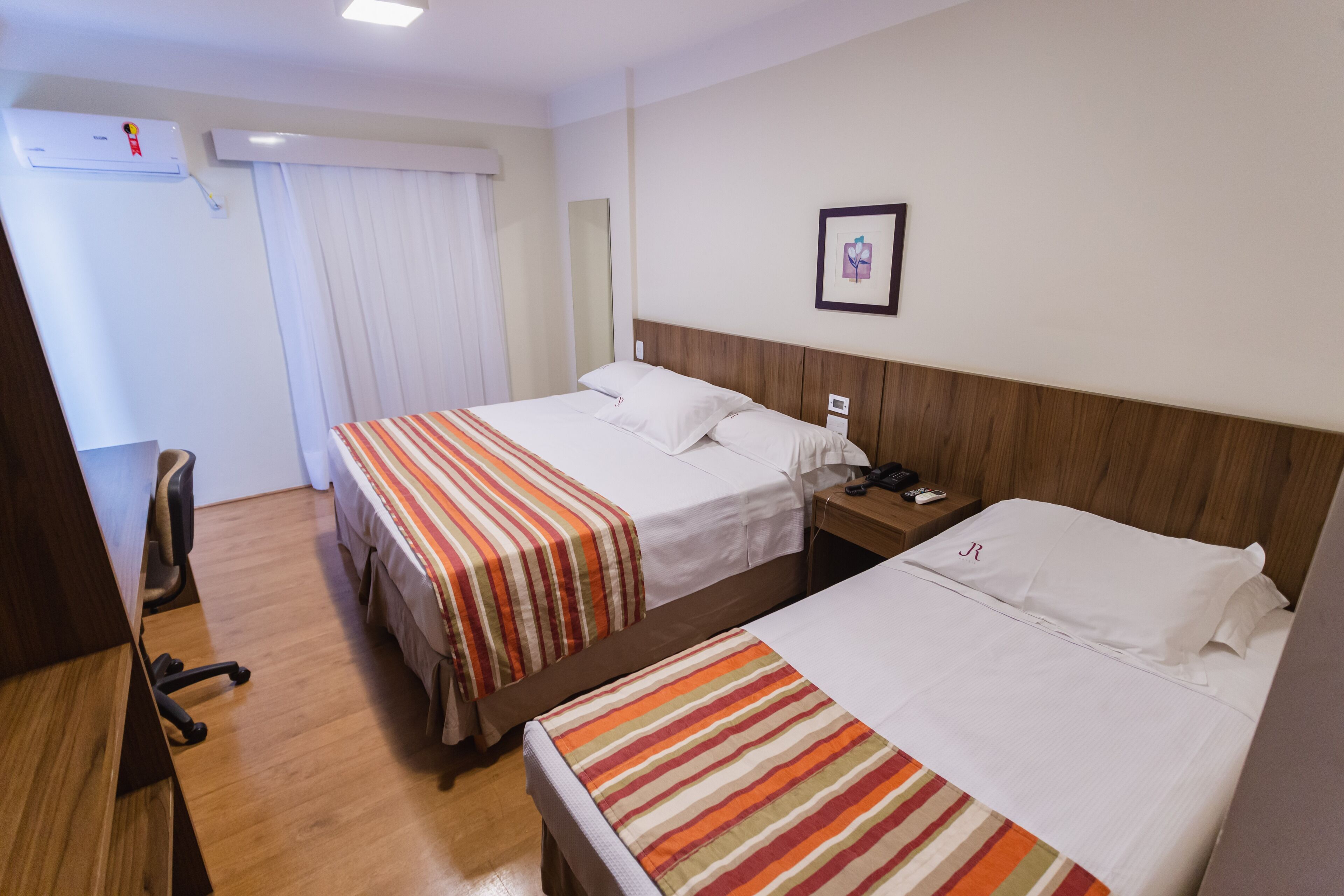 Een hotelkamer met twee bedden, een bureau, een stoel en een nachtkastje met een lamp.