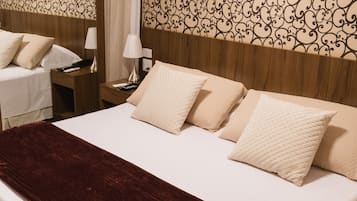 Ein ordentlich bezogenes Bett mit einer dunkelroten Decke, ein Holzkopfschild mit einem gemusterten Design und ein Nachttisch mit Lampe und Fernbedienung.
