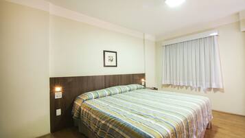 Habitación de hotel con cabecera de madera, cubrecama a rayas, un cuadro enmarcado en la pared y una ventana con cortinas.