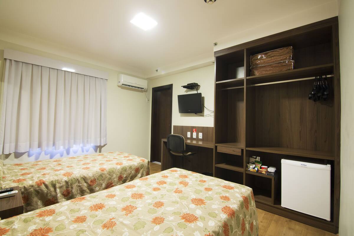 Camera d'albergo con due letti, una scrivania, una sedia, una televisione e un armadio.