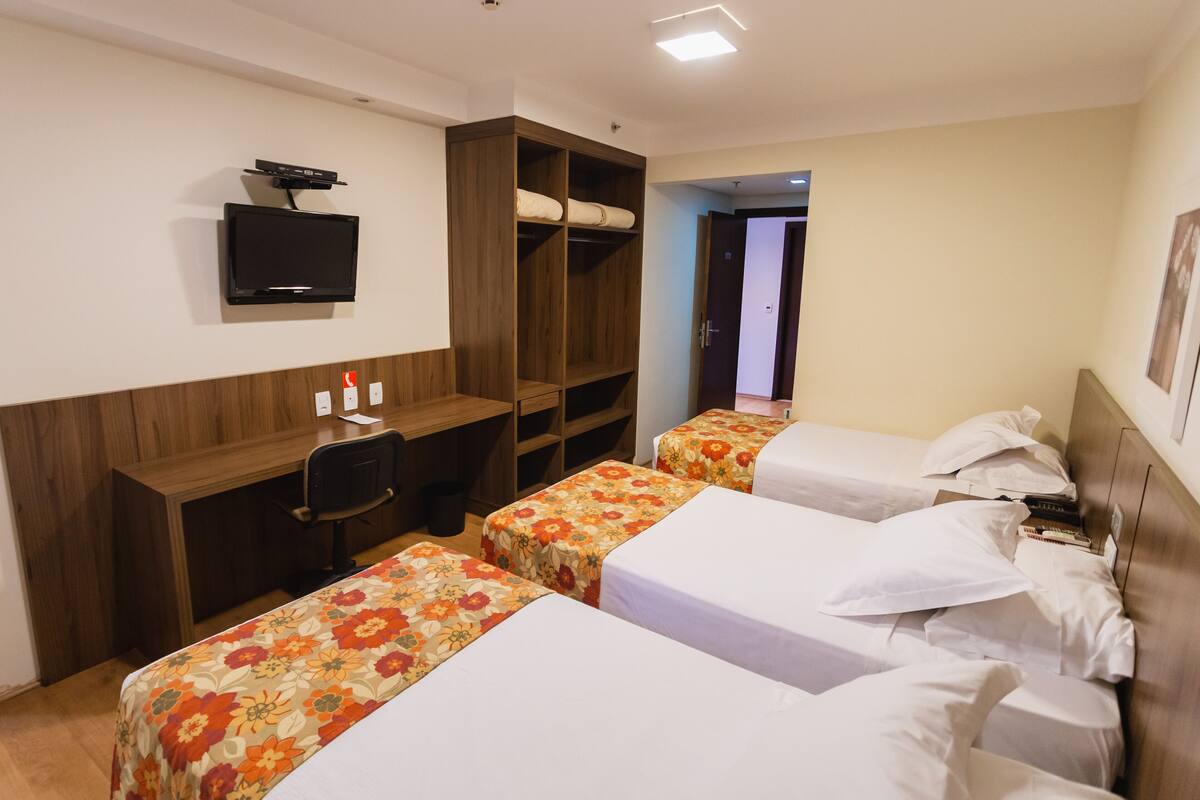 Una camera d'albergo con due letti, una scrivania, una televisione e un armadio.