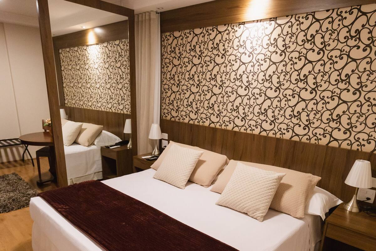 Un letto rifatto con cura, una coperta scura, una testiera in legno e una carta da parati decorata.