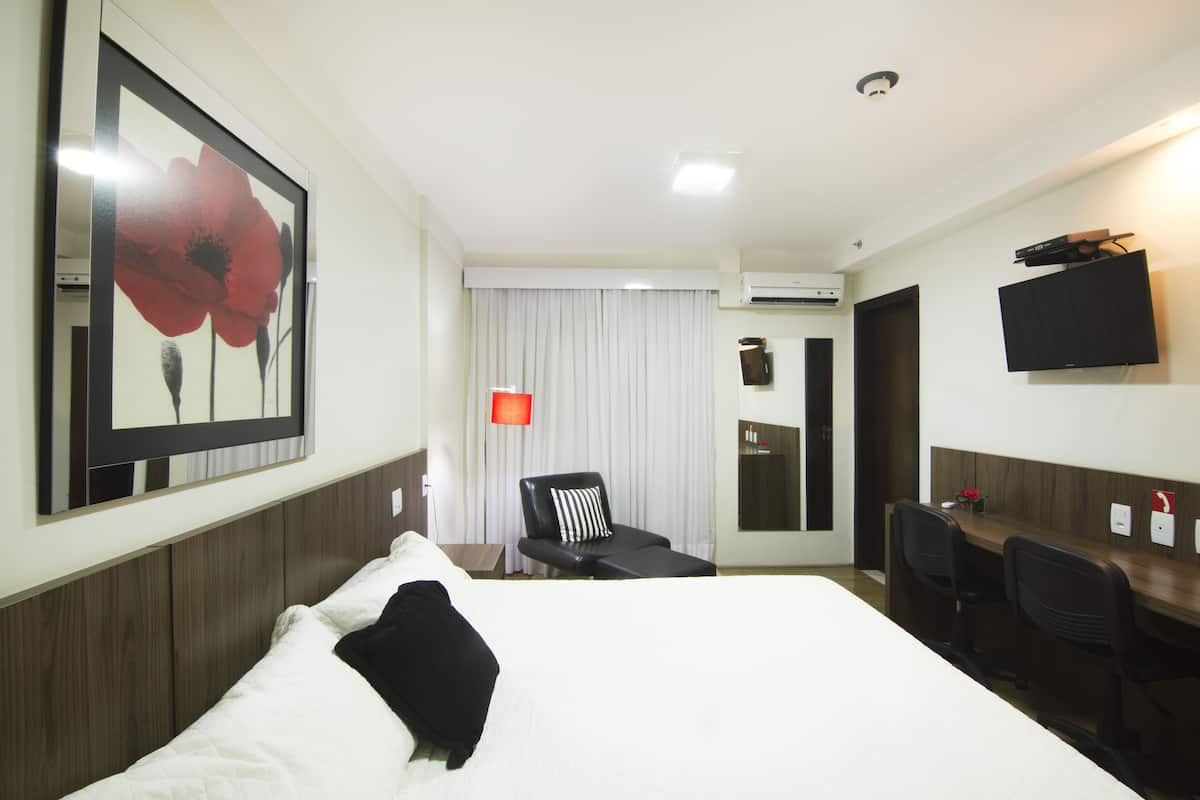 Una camera d'albergo con un letto grande, una scrivania con sedie, una televisione e un condizionatore.