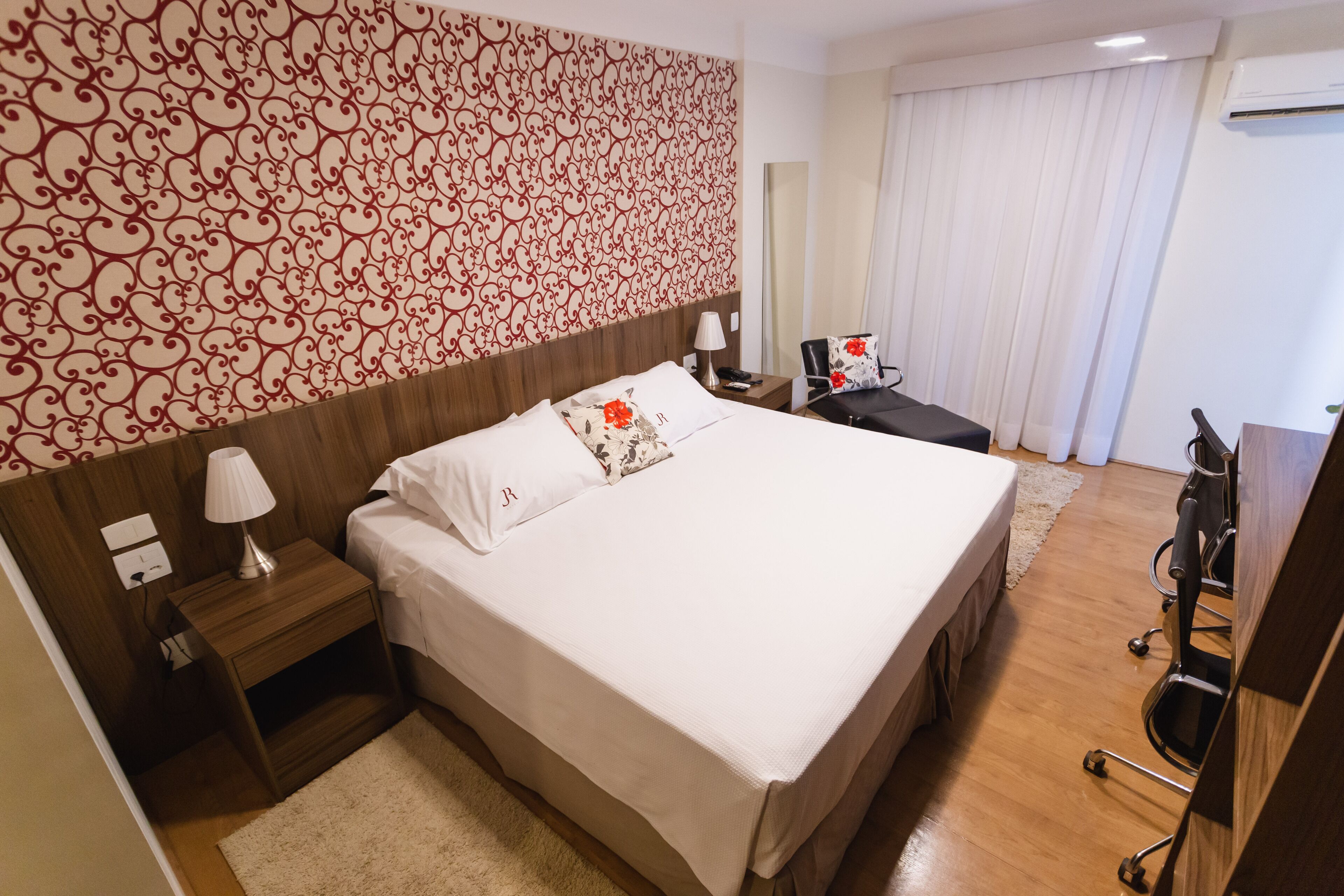 Habitación de hotel con una cama grande, cabecera de madera, mesita de noche con lámpara, escritorio con silla y un espejo amplio.