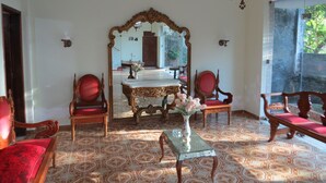 A room with a large ornate mirror, a wooden table with a vase of flowers, and red upholstered chairs. - Charitas Inn (Niteroi)