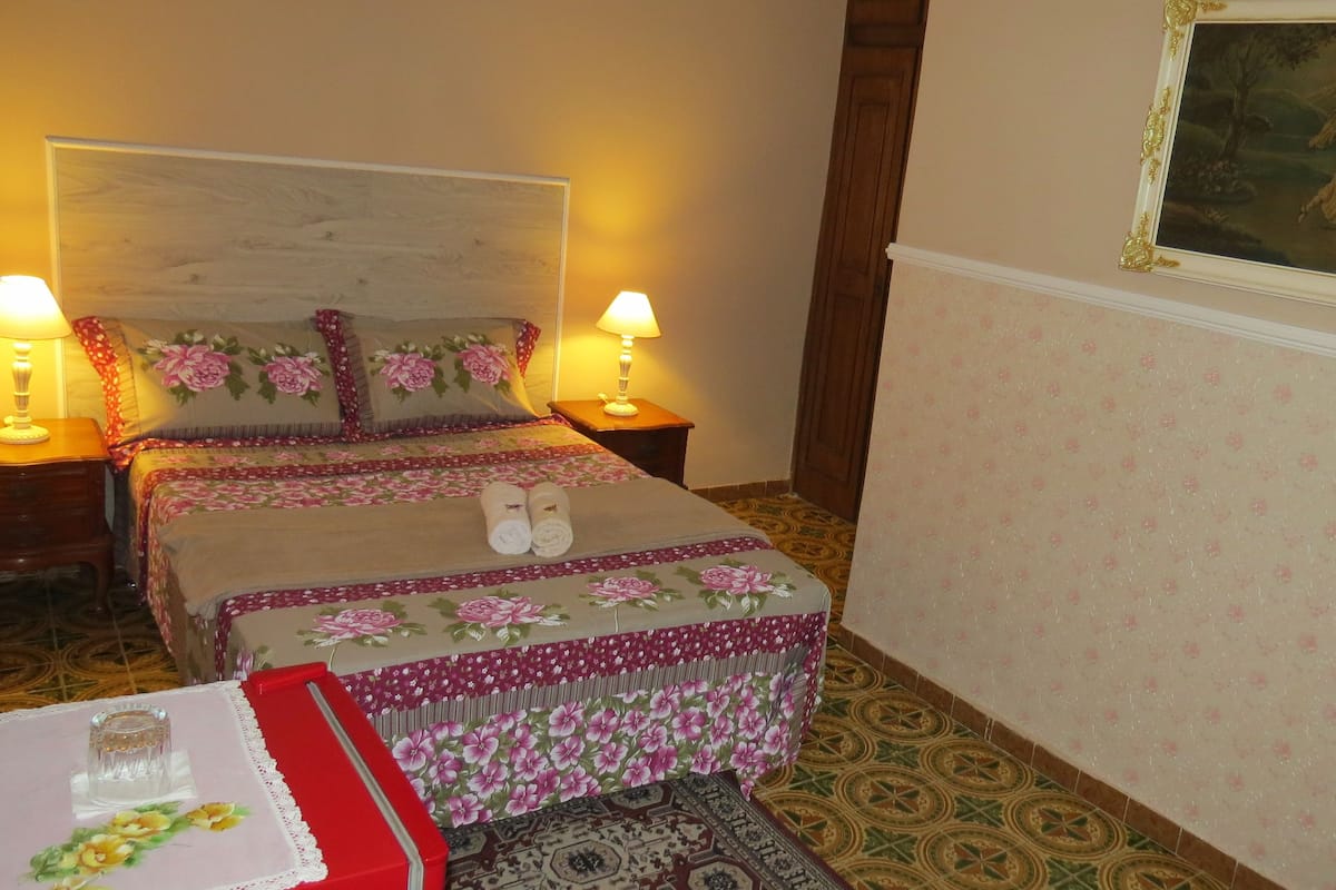 A hotel room with two beds, floral bedding, a painting on the wall, and a patterned floor.