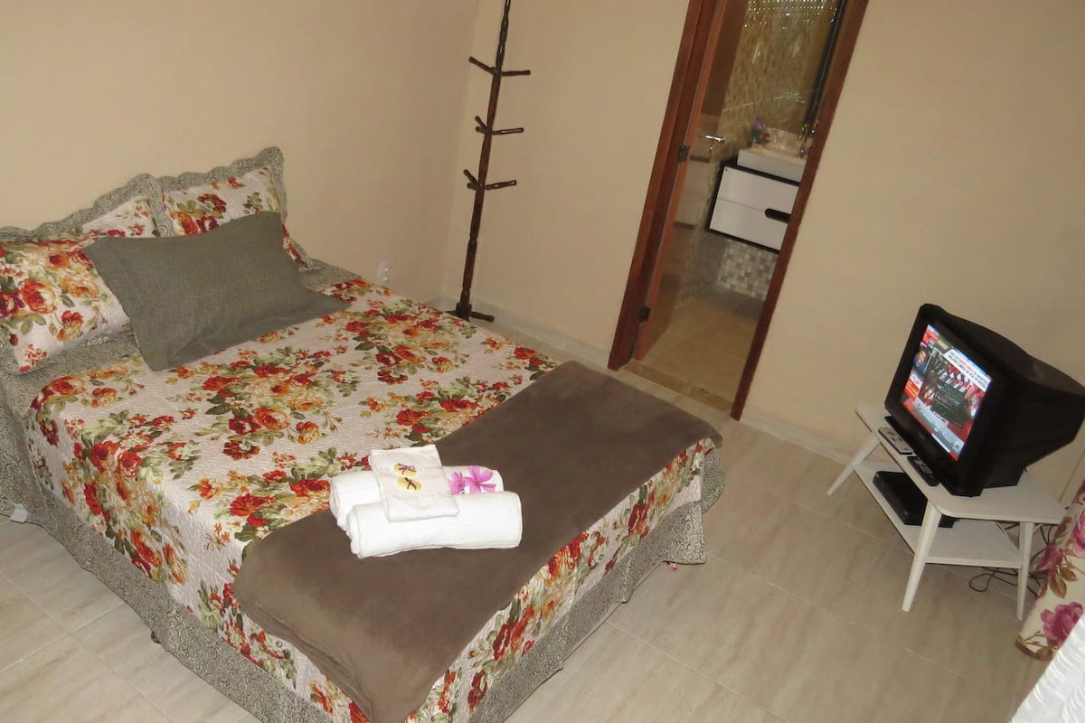 A neatly made bed with floral bedding, a bedside lamp, and a television on a stand.