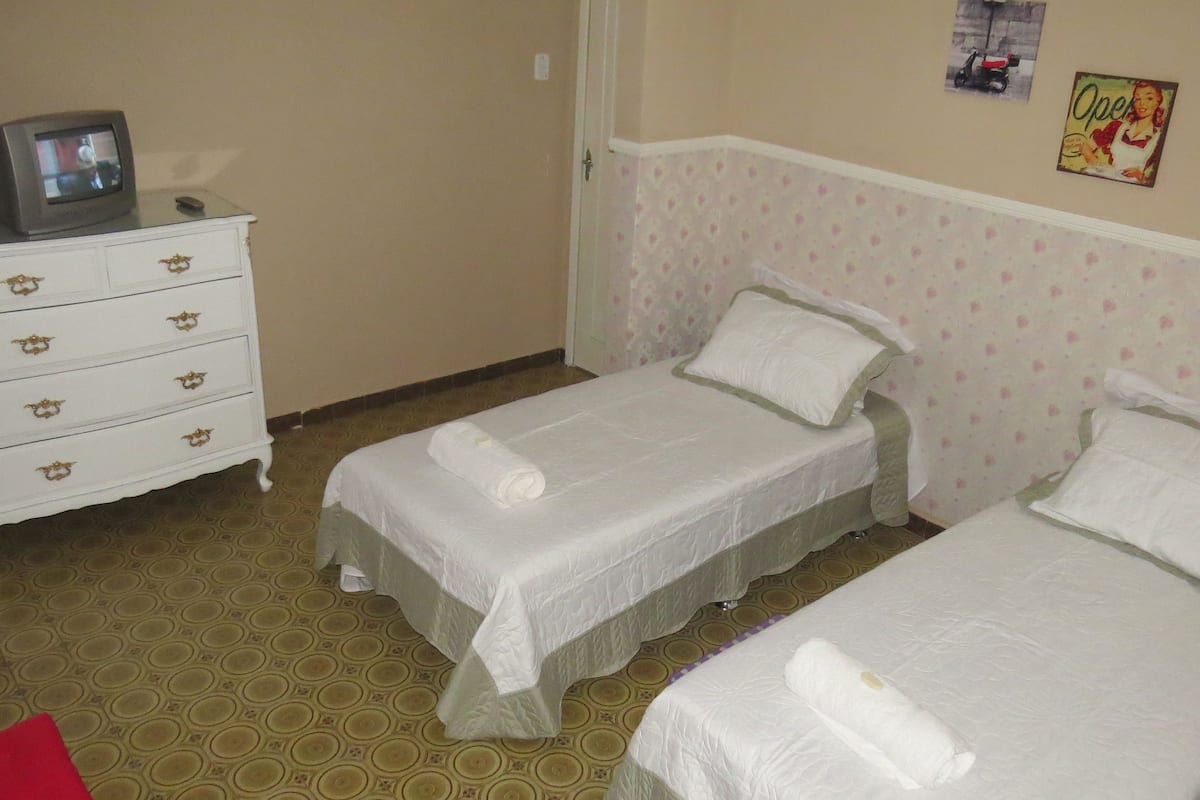 A hotel room with two single beds, a white dresser with drawers, a television on top, and a patterned carpet.