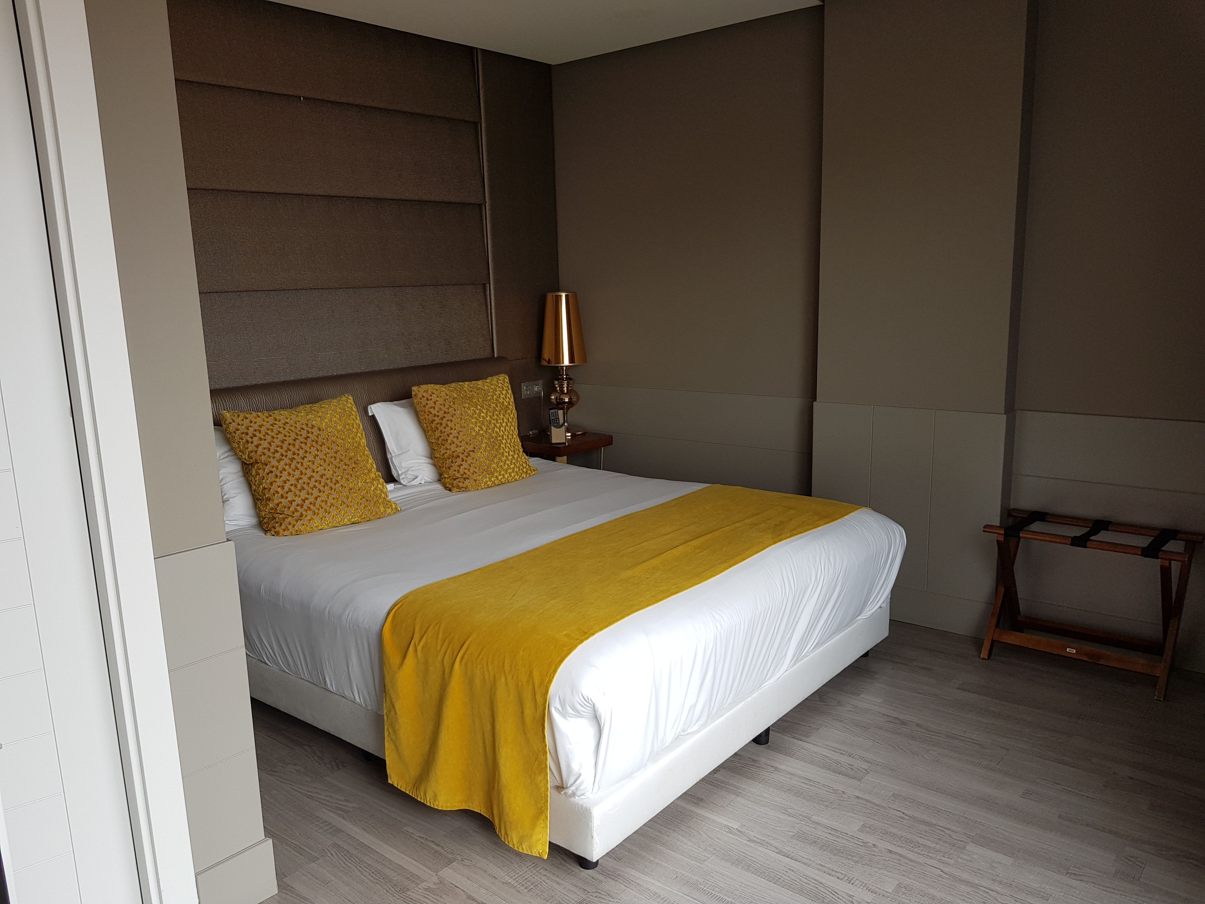 Een moderne hotelkamer met een groot bed, een nachtkastje met een lamp en een houten bankje.