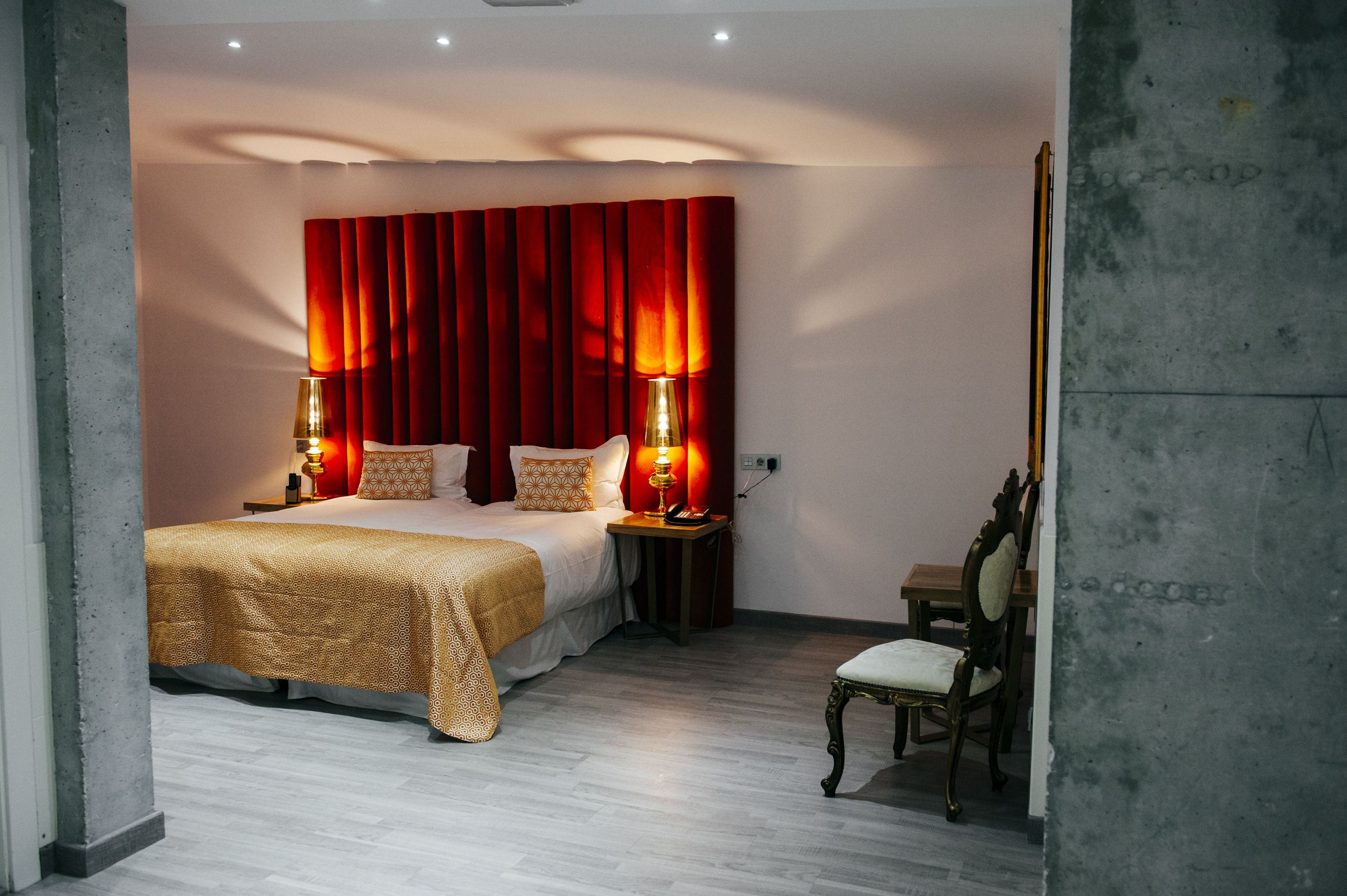 A hotel room with a bed, two bedside lamps, a nightstand, a chair, and a wooden table.