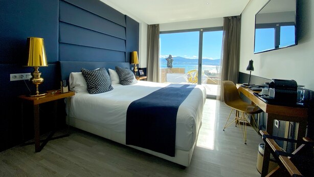 Quarto de hotel com uma cama grande, uma escrivaninha e vista para o mar.
