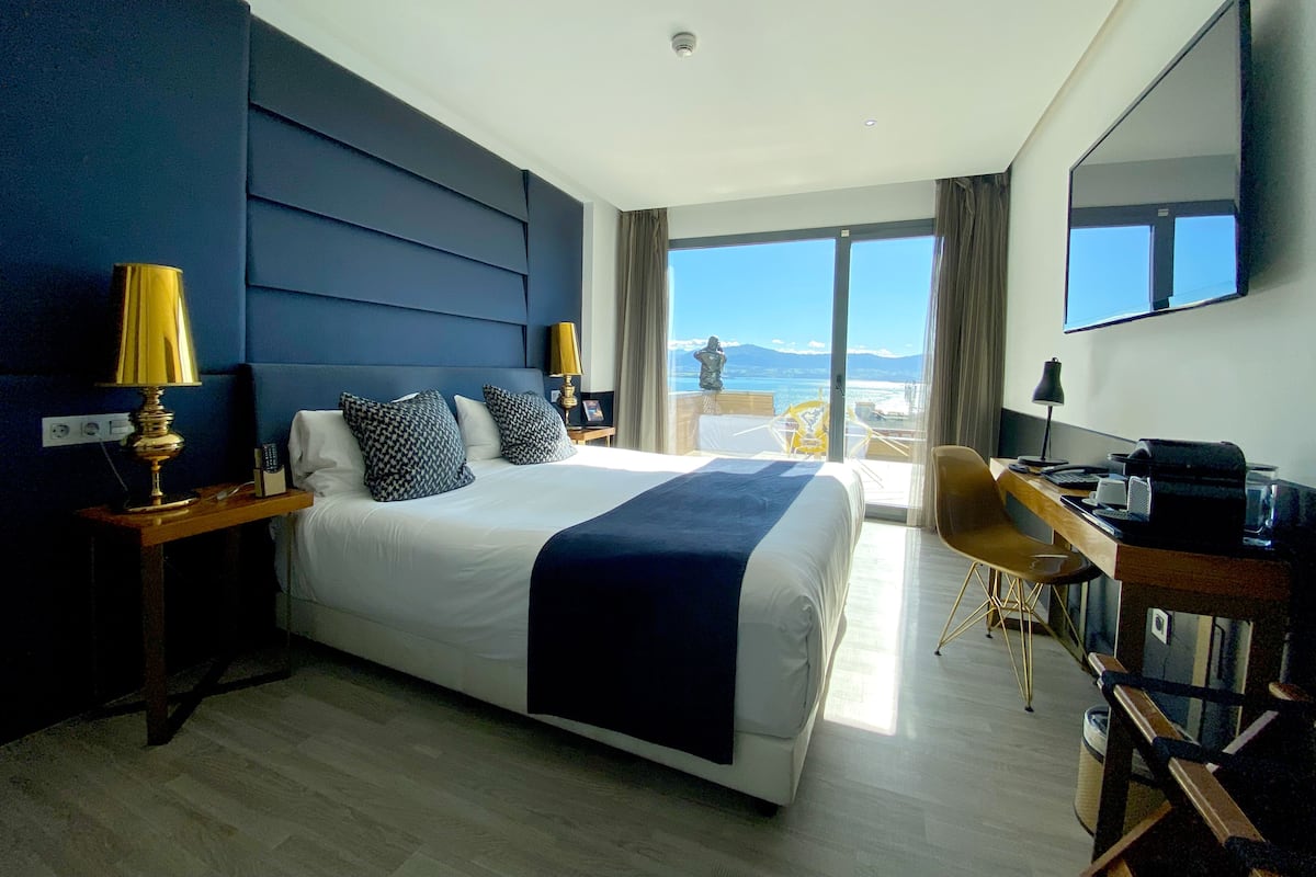 A hotel room with a large bed, a desk, and a view of the sea.