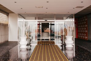Entrada de hotel con puerta de cristal, suelo estampado y pared roja con flechas blancas.