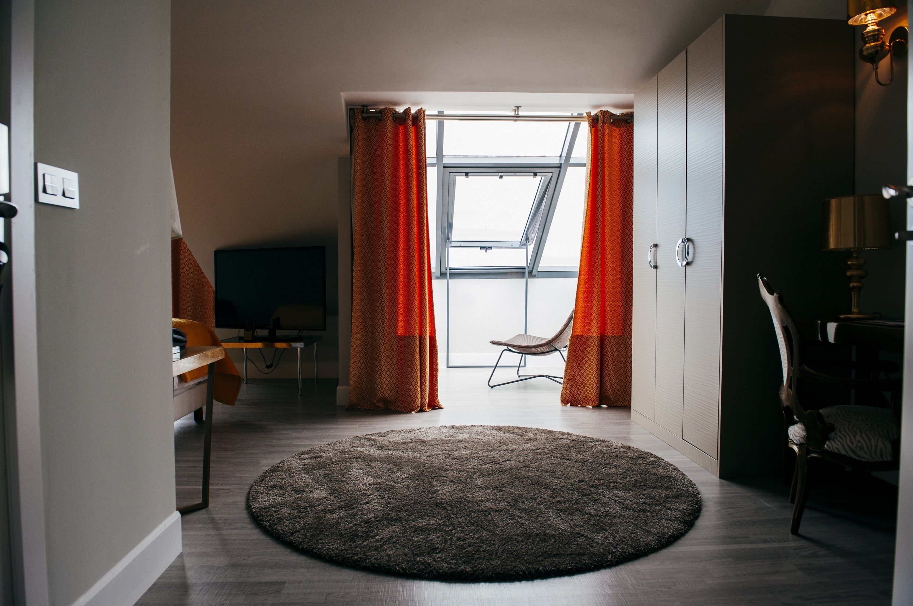 A modern room with a large window, a round rug, a chair, and a desk.