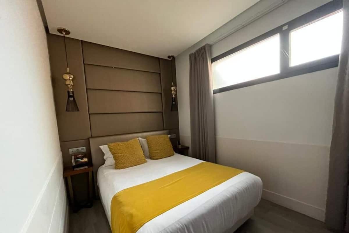 A hotel room with a bed, a nightstand, a lamp, and a window with curtains.