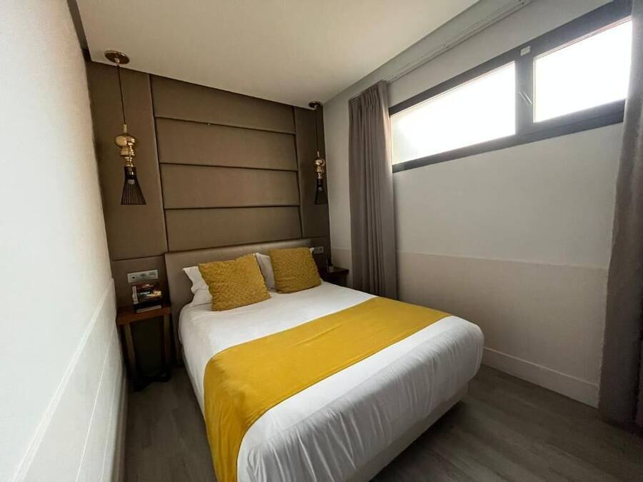 A hotel room with a bed, a nightstand, a lamp, and a window with curtains.