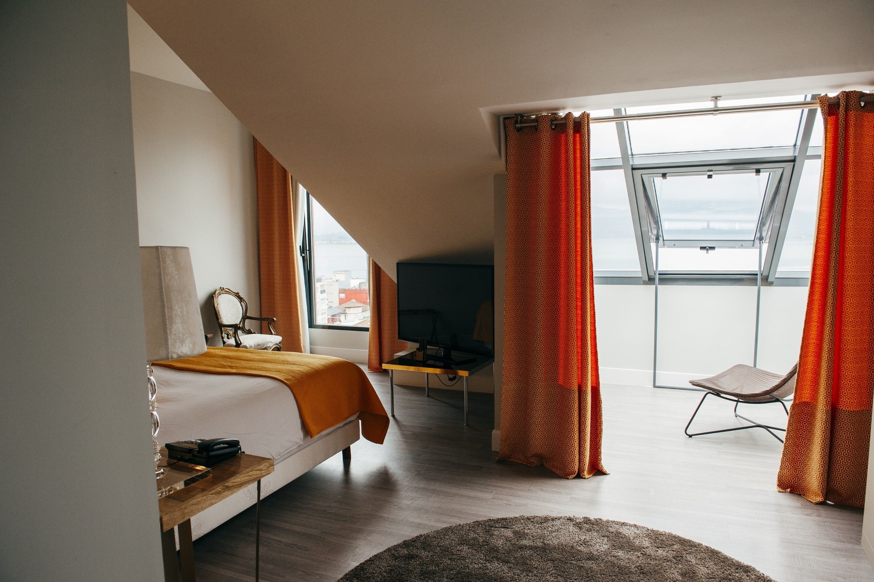 Un dormitorio moderno con cama, escritorio, silla y un ventanal con cortinas.