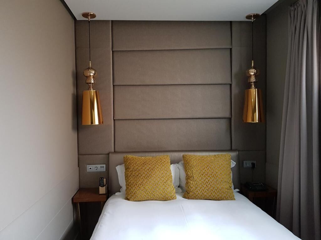 A hotel room with a large bed, two bedside tables, a headboard with horizontal panels, and two wall-mounted lamps.