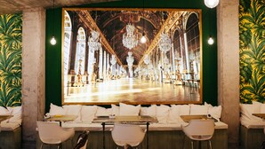 Restaurante com um grande mural de um salão imponente, assentos brancos e lâmpadas penduradas.